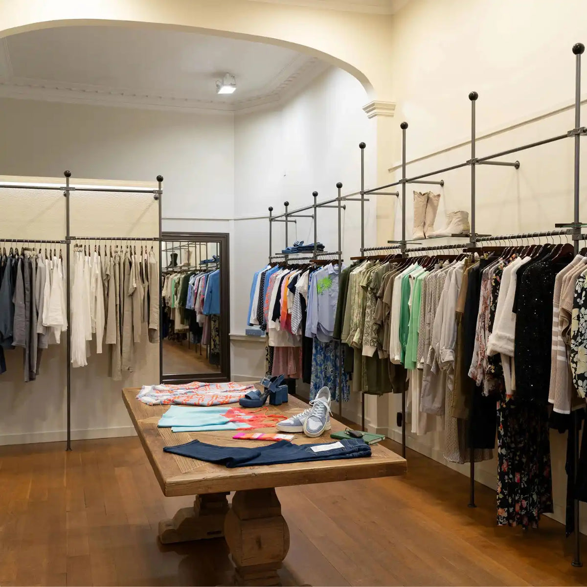 Wooden display table with folded clothing surrounded by hanging garment racks.